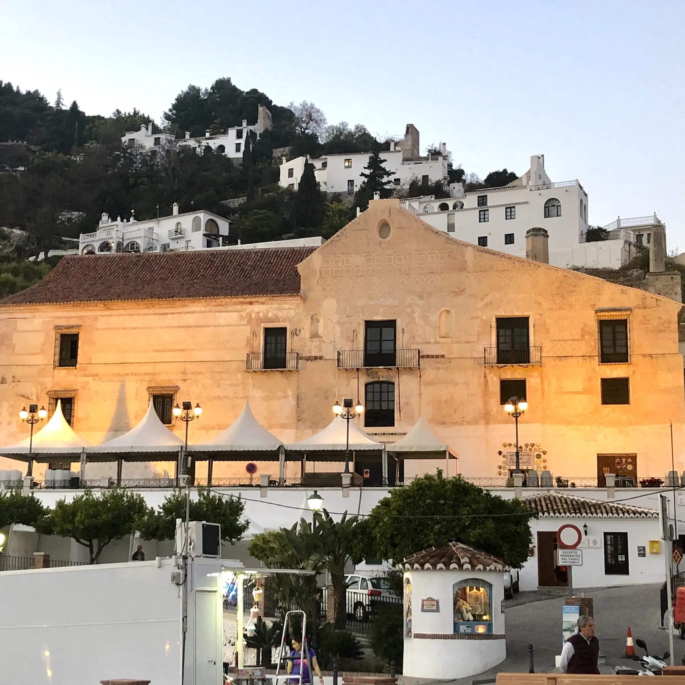 Casa del Apero, the historic sugar warehouse at the foot of Frigiliana's old town, lit up at dusk with the white village rising behind.